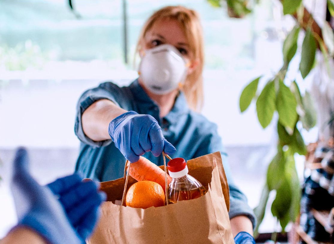 Women handing a bag of food supplies wearing protective equipment
