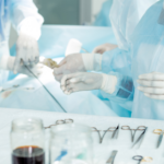 Surgeons in blue sterile gowns performing surgery with tools on a sterile table laid out nearby showin hands in gloves.