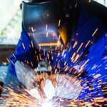 Welder in protective gear welding metal, bright sparks flying around in an industrial workshop