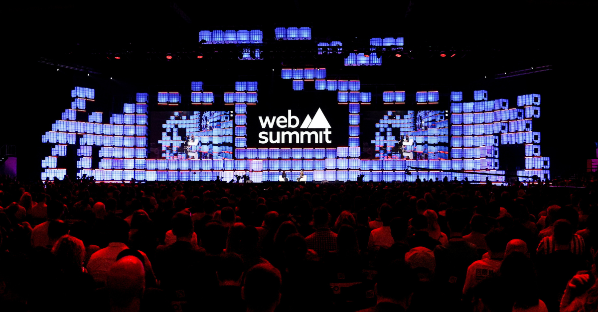 Large concert-style stage with blue lit square panels and the 'web summit' logo; audience in foreground looking toward the stage.