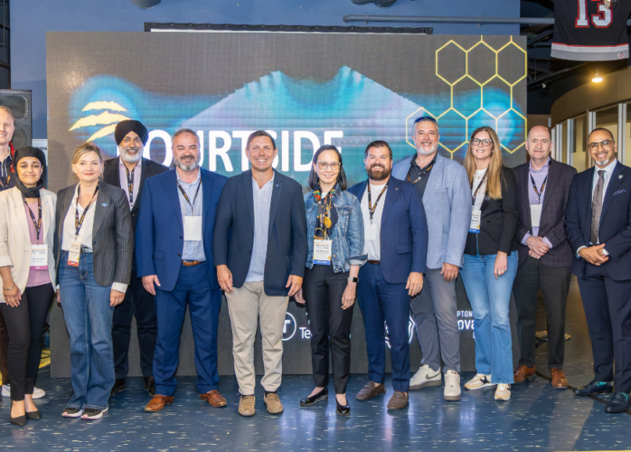 Group of diverse professionals posing for a photo at a conference, in front of a large digital screen backdrop with hexagon graphics.
