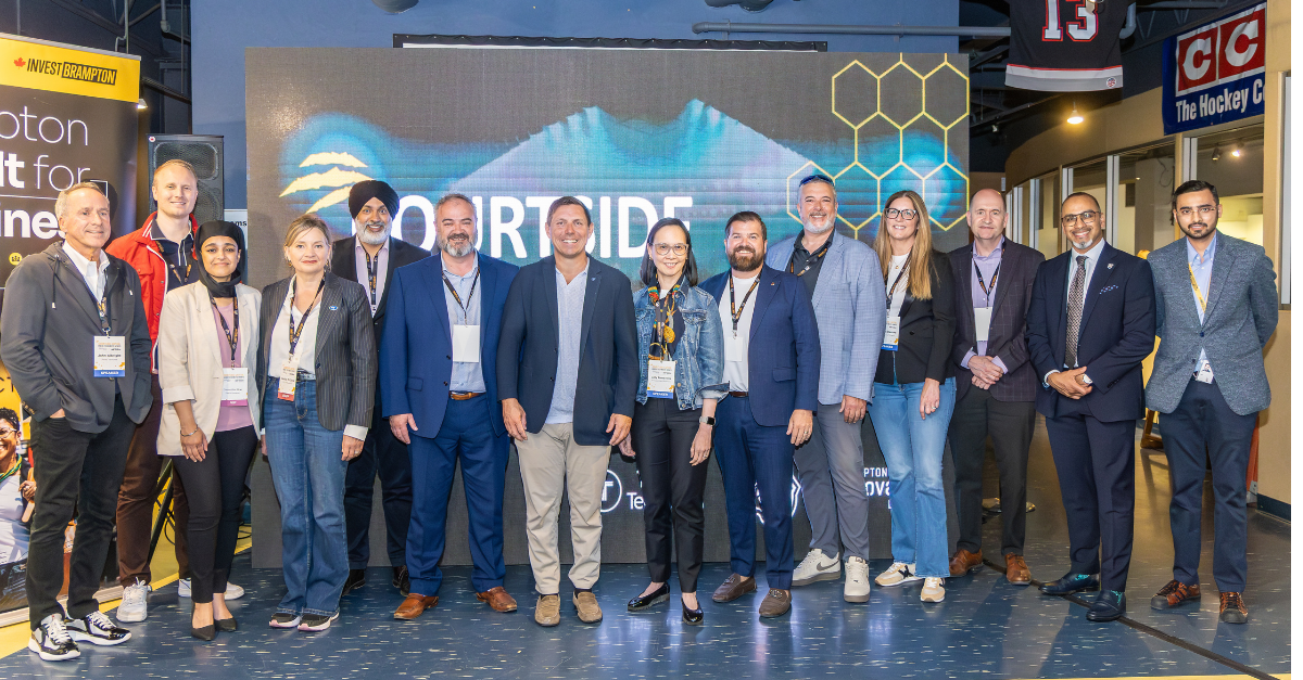 Group of diverse professionals posing for a photo at a conference, in front of a large digital screen backdrop with hexagon graphics.