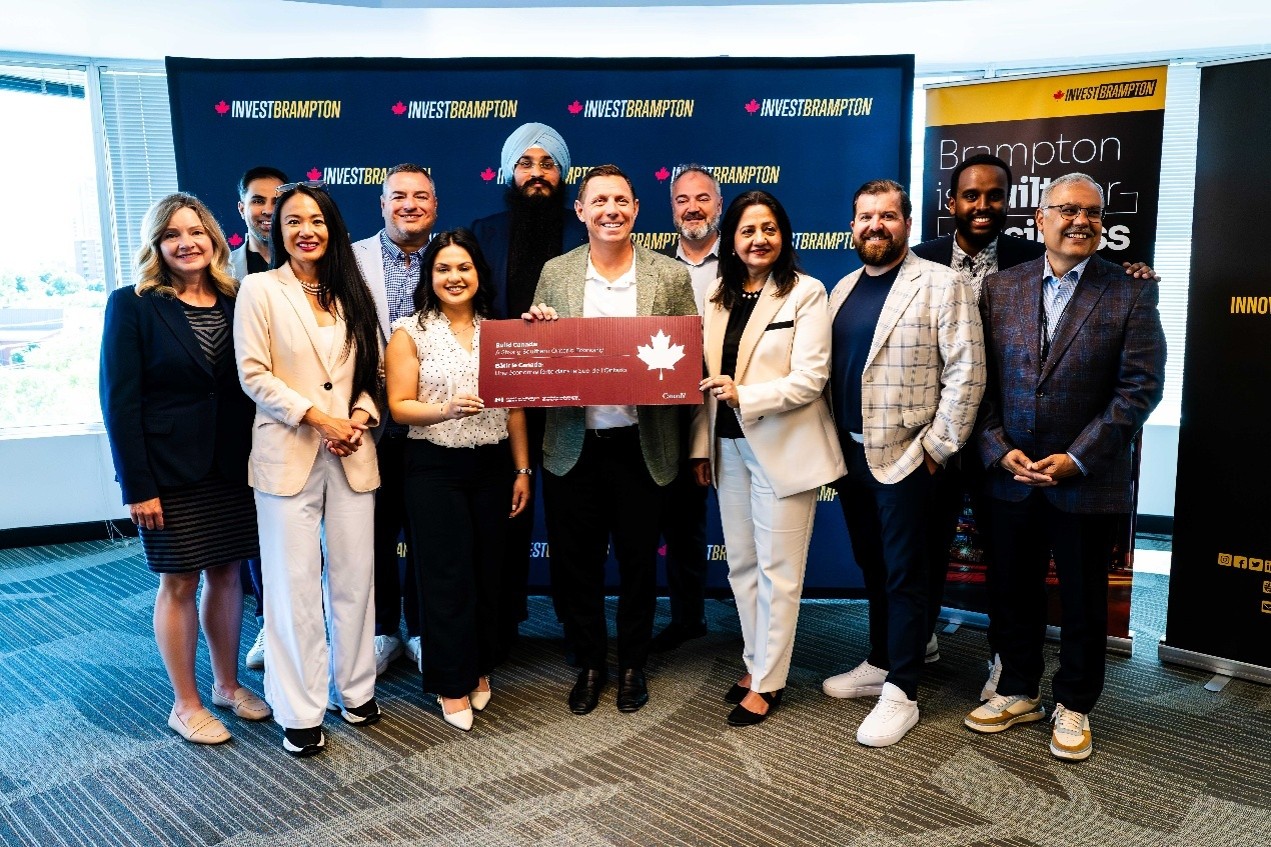 Group of professionals posing in an office, holding a large red ceremonial cheque at an Invest Brampton event