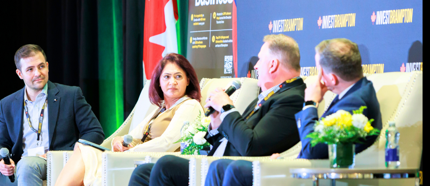 Four panelists seated in cream chairs on a stage, microphones in hand, with a blue Invest Brampton backdrop and a Canadian flag nearby.