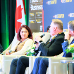 Four panelists seated in cream chairs on a stage, microphones in hand, with a blue Invest Brampton backdrop and a Canadian flag nearby.