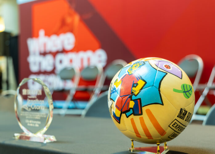 Colorful patterned soccer ball on a stand in a trophy display, with a blurred red backdrop in the background.