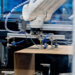 Industrial robotic arm operating over a cardboard box on a conveyor in a factory automation setup, performing packaging tasks