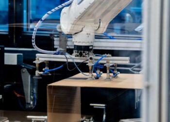Industrial robotic arm operating over a cardboard box on a conveyor in a factory automation setup, performing packaging tasks