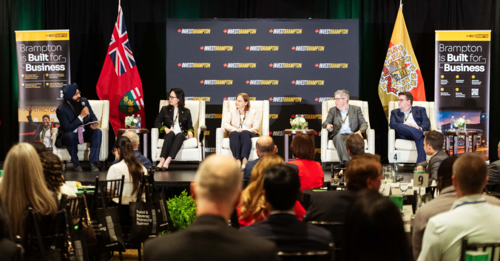 Brampton Food Summit 2026 Crowd - Invest Brampton | Brampton Economic Development Panel discussion on stage with five speakers, Brampton business banners, and flags, addressing an audience.