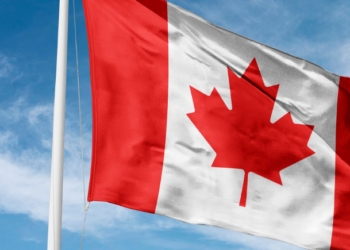 Canadian flag waving on a flagpole against a bright blue sky