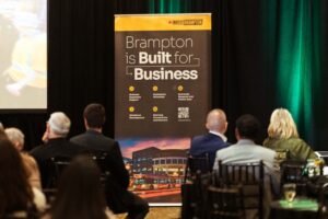 Brampton_Food and Bev Summit_D85_8859 - Invest Brampton | Brampton Economic Development Audience seated at a conference facing a tall banner reading'Brampton is Built for Business' on stage.