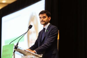 Brampton_Food and Bev Summit_D85_8945 - Invest Brampton | Brampton Economic Development Man in a dark suit giving a speech at a podium with two microphones in front of a large screen, conference setting