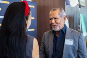 Brampton_Food and Bev Summit_Z62_0296 - Invest Brampton | Brampton Economic Development Older man in a gray blazer conversing with a woman wearing a red headband at a networking event backdrop