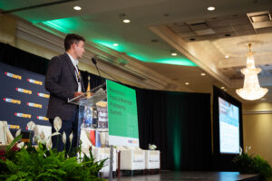 Brampton_Food and Bev Summit_Z62_0329 - Invest Brampton | Brampton Economic Development Speaker at a podium giving a presentation at a Brampton conference, with green signage and a backdrop reading Invest Brampton.”