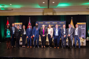 Brampton_Food and Bev Summit_Z62_0442 - Invest Brampton | Brampton Economic Development Group of professionals in business attire posing on a stage for a photo at a conference, with flags and banners in the background (Invest Brampton banners).