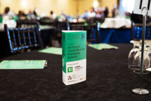 Brampton_Food and Bev Summit_Z62_9772 - Invest Brampton | Brampton Economic Development Teal conference brochure standing upright on a black table at a blurred banquet setting.