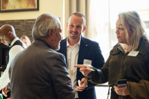 Brampton_Food and Bev Summit_Z62_9820 - Invest Brampton | Brampton Economic Development Professionals at a networking event converse; man in a blue blazer smiles as a woman offers a business card and coffee cup nearby.