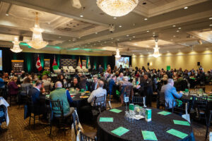 Brampton_Food and Bev Summit_Z62_9835 - Invest Brampton | Brampton Economic Development Large conference banquet hall with round tables, teal program booklets, and a stage with flags and banners in the background.
