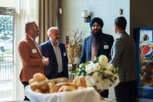 Brampton_Food and Bev Summit_Z62_9906 - Invest Brampton | Brampton Economic Development Four men in business attire chat by a table of pastries in a bright room, with a Pepsi vending machine visible in the background.