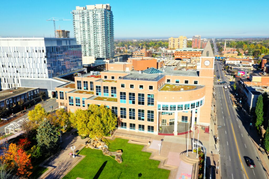 Aerial view of a modern city center with glass office buildings, a clock tower, and a green park in the foreground.