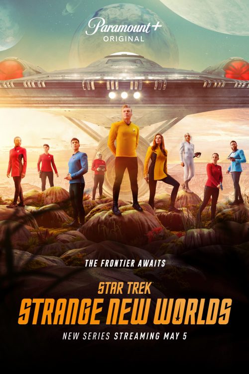 Promotional Star Trek poster: diverse crew in colorful uniforms on rocky alien terrain, with a large starship and planets in the sky.